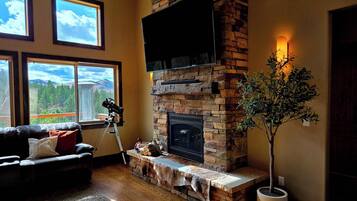 A living room with a fireplace, a telescope, and a large window with a mountain view.
