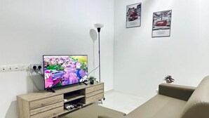 A modern living room with a flat-screen TV on a wooden TV stand, a beige sofa, and a floor lamp. - Setia Tri-Suite(3) by Homey Planet (Bayan Lepas)