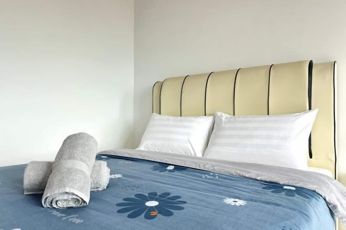 A neatly made bed with a blue floral bedspread, white pillows, and rolled towels.
