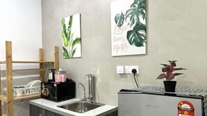 A compact kitchen with a sink, a microwave, and a refrigerator. There are two framed artworks on the wall, one depicting green leaves and the other with the phrase "Love Lives Here". A potted plant is on the counter. - Setia Tri-Suite(3) by Homey Planet (Bayan Lepas)