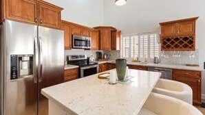 A modern kitchen with wooden cabinets, stainless steel appliances, a marble countertop, and a large window providing natural light. - Ahwatukee Adventures Family Home + Pool (Phoenix)