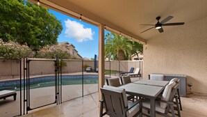 An outdoor patio with a pool, a table and chairs, a ceiling fan, and a view of the surrounding area. - Ahwatukee Adventures Family Home + Pool (Phoenix)