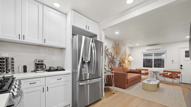 A modern kitchen with white cabinets, a stainless steel refrigerator, and a coffee maker. - Designer 2BR in Prime Location w/ Outdoor Dining! (San Diego)