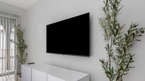 Una sala moderna con un mueble bajo blanco, un televisor montado y dos plantas en macetas.