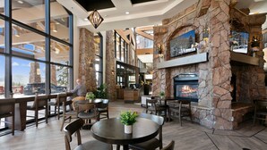 A spacious indoor area with a stone fireplace, wooden furniture, and large windows offering views of the outdoors. - Summer! Mountain Views Balcony Multiple Pools Golf Tennis Hiking Resort Perfection! (Park City)