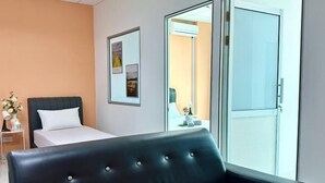 A modern hotel room with a bed, a black leather sofa, a small table with a vase of flowers, and a framed picture on the wall. - Setia Tri-Suite(2) by Homey Planet (Bayan Lepas)