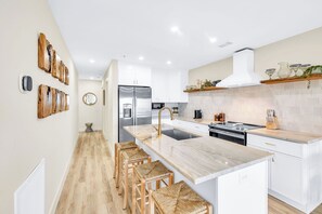Una cocina moderna con armarios blancos, encimera de mármol y refrigerador de acero inoxidable.