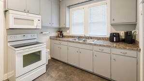 A compact kitchen with white appliances, a granite countertop, and a window with blinds. - Stylish 2BR Near ECU Health, ECU & Downtown • Fast WiFi (Greenville)