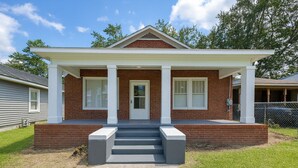 A two-story house with a front porch, a brick facade, and a white door. - Stylish 2BR Near ECU Health, ECU & Downtown • Fast WiFi (Greenville)
