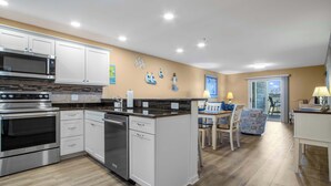A modern kitchen with stainless steel appliances, white cabinetry, and a dining area with a table and chairs. - Harbour Club A5 (Ocean City)