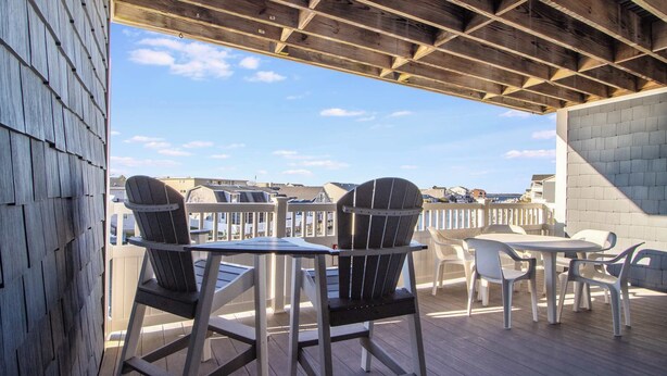 An outdoor deck with wooden flooring, metal-framed chairs, and a white table. - Harbour Club A5 (Ocean City)