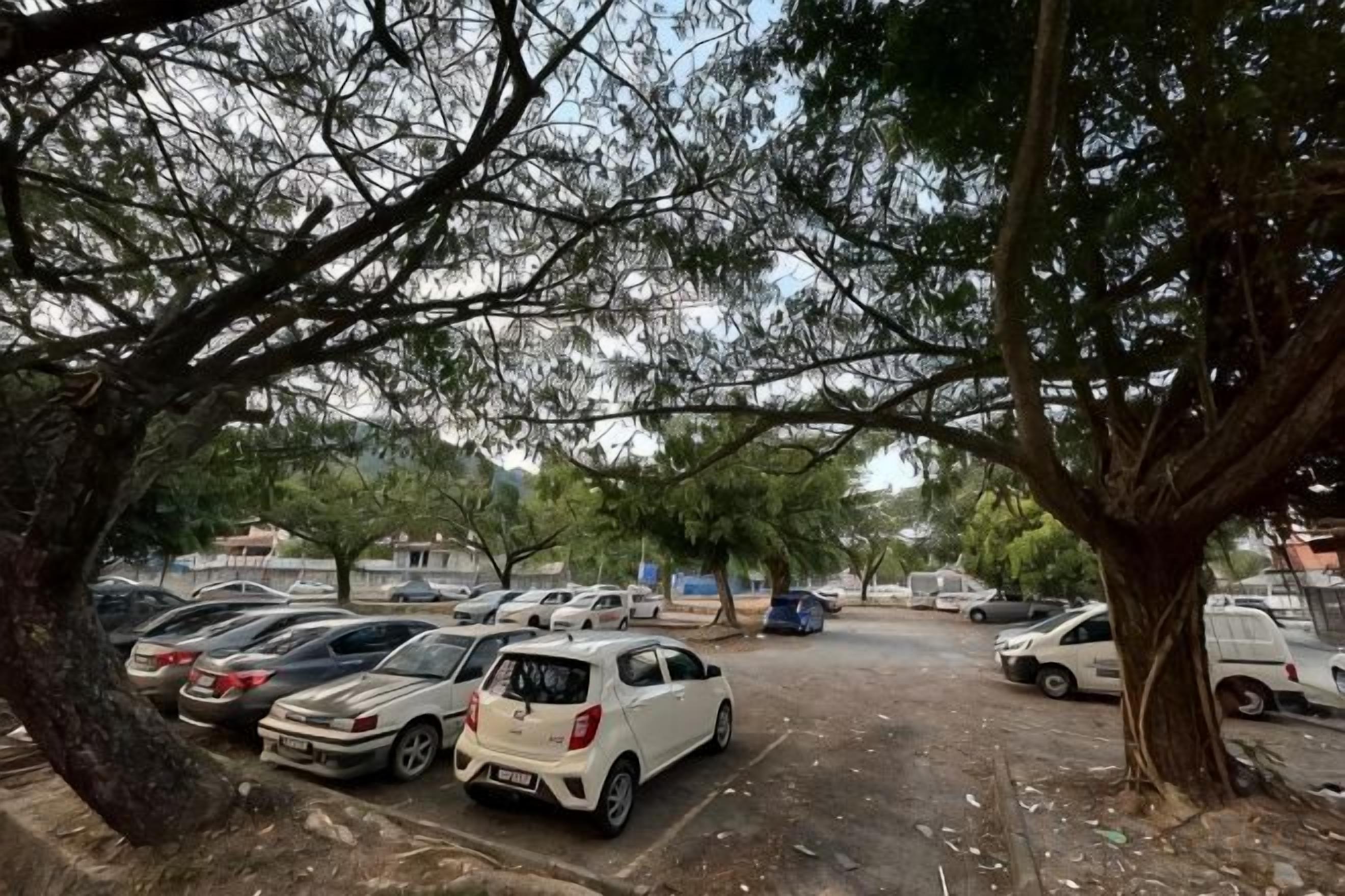 A parking lot with multiple cars and trees providing shade.