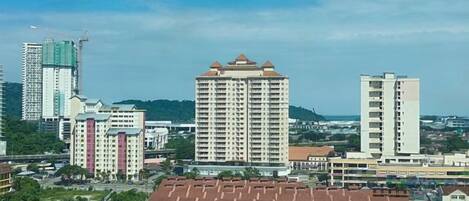 A high-rise building with a flat roof and multiple balconies, surrounded by other buildings and greenery.