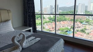 Ein Hotelzimmer mit großem Fenster, einem Bett mit weißer Bettwäsche und Blick auf Gebäude und Grünflächen.
