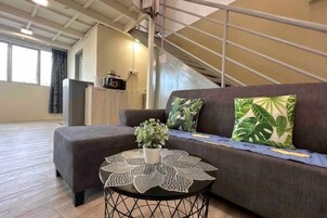 Una sala de estar con un sofá, una mesa de centro con una planta y una escalera al fondo.