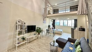 Ein großzügiger Wohnbereich mit Fernseher, Bücherregal und Sitzgelegenheiten. Im Hintergrund ist ein Balkon zu sehen.