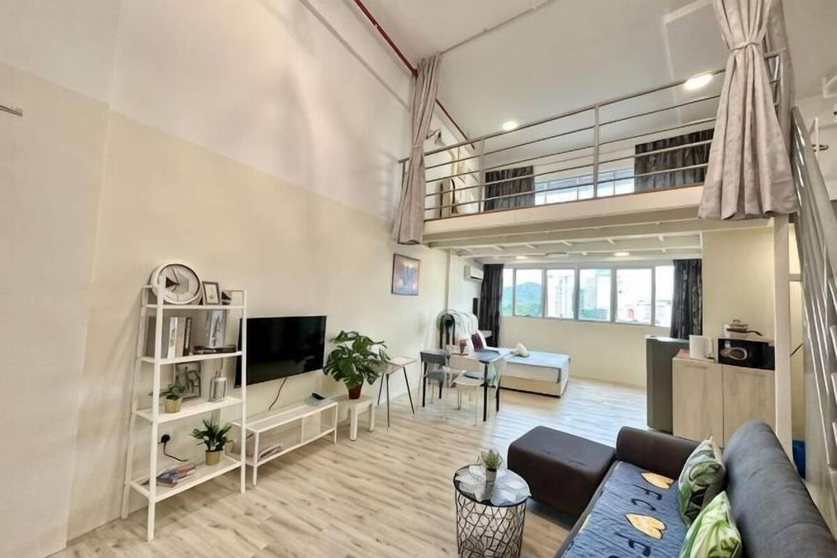 A spacious living area with a TV, bookshelf, and seating. A balcony is visible in the background.