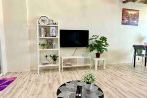Un soggiorno con televisore, libreria, piante in vaso e un tavolino rotondo.