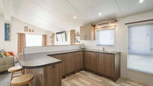 Una cocina moderna con armarios de madera, encimera de granito y un lavamanos integrado. Se observa una ventana con persianas, un taburete pequeño y un adorno en la pared.
