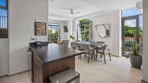 A modern kitchen with a central island, dining area with chairs, and large windows offering views of greenery. - Galeritas 5 | 2BR/2BA in Puerto Vallarta w/ pool (Puerto Vallarta)