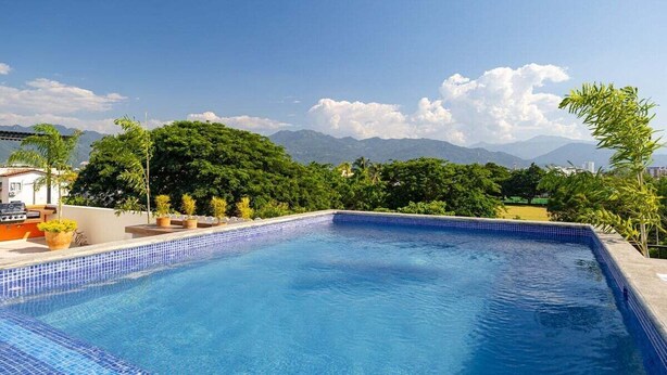 A swimming pool with a tiled edge, surrounded by greenery and mountains in the background. - Galeritas 5 | 2BR/2BA in Puerto Vallarta w/ pool (Puerto Vallarta)