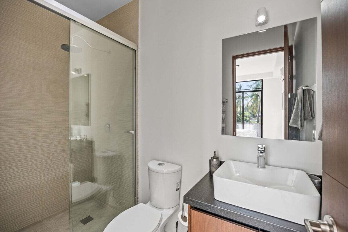 Een moderne badkamer met een glazen douchecabine, een wit toilet, een grote wastafel met spiegel en een handdoek aan de muur.
