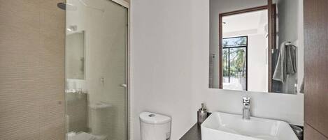 Een moderne badkamer met een glazen douchecabine, een wit toilet, een grote wastafel met spiegel en een handdoek aan de muur.