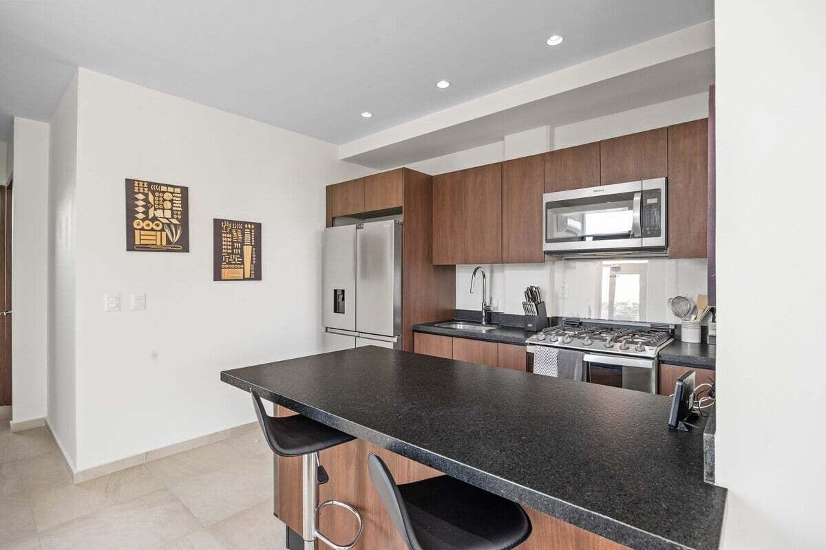 A modern kitchen with dark countertops, stainless steel appliances, and wooden cabinets.