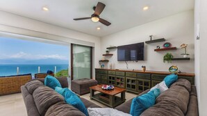 Ein modernes Wohnzimmer mit Sofa, Couchtisch und Fernseher, mit Blick auf eine schöne Küstenlandschaft.