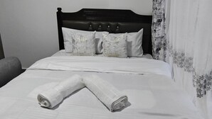 Ein ordentlich bezogenes Bett mit weißen Laken, einem schwarzen Kopfteil und blumigen Vorhängen.