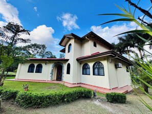 A two-story building with a red-tiled roof, arched windows, and a stone archway entrance. - Arenal: A Tropical Home (La Fortuna)
