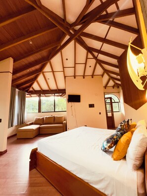 A spacious bedroom with a large bed, a sofa bed, and a ceiling with wooden beams. - Arenal: A Tropical Home (La Fortuna)