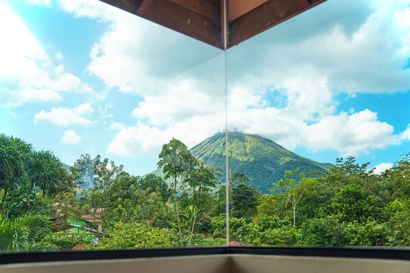 A view of a lush green landscape with a mountain in the background, viewed through a window with a metal frame. - Arenal: A Tropical Home (La Fortuna)