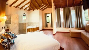 Un dormitorio amplio con una cama grande, vigas de madera en el techo, un baño con pared de mármol y vistas al exterior a través de una ventana.