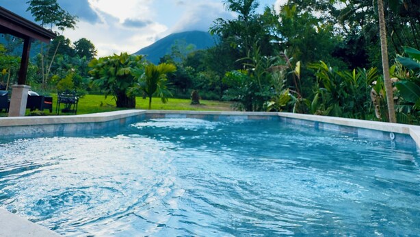 Una piscina con agua azul cristalina, rodeada de exuberante vegetación y una montaña al fondo.