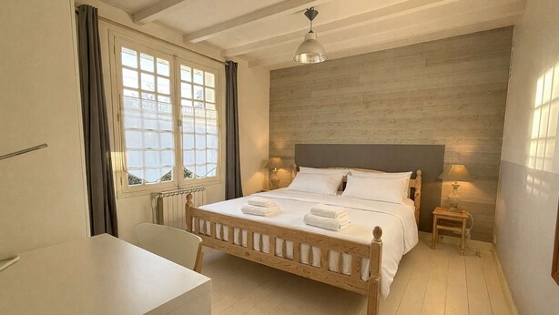 Camera da letto con un letto in legno, un tavolo, una sedia, una finestra con tende e un muro con motivo decorativo.