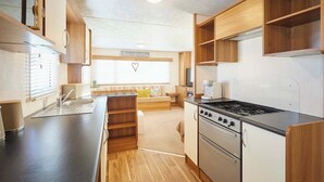 Una cocina compacta con estufa, horno y pileta, armarios de madera y un ventanal con persianas.