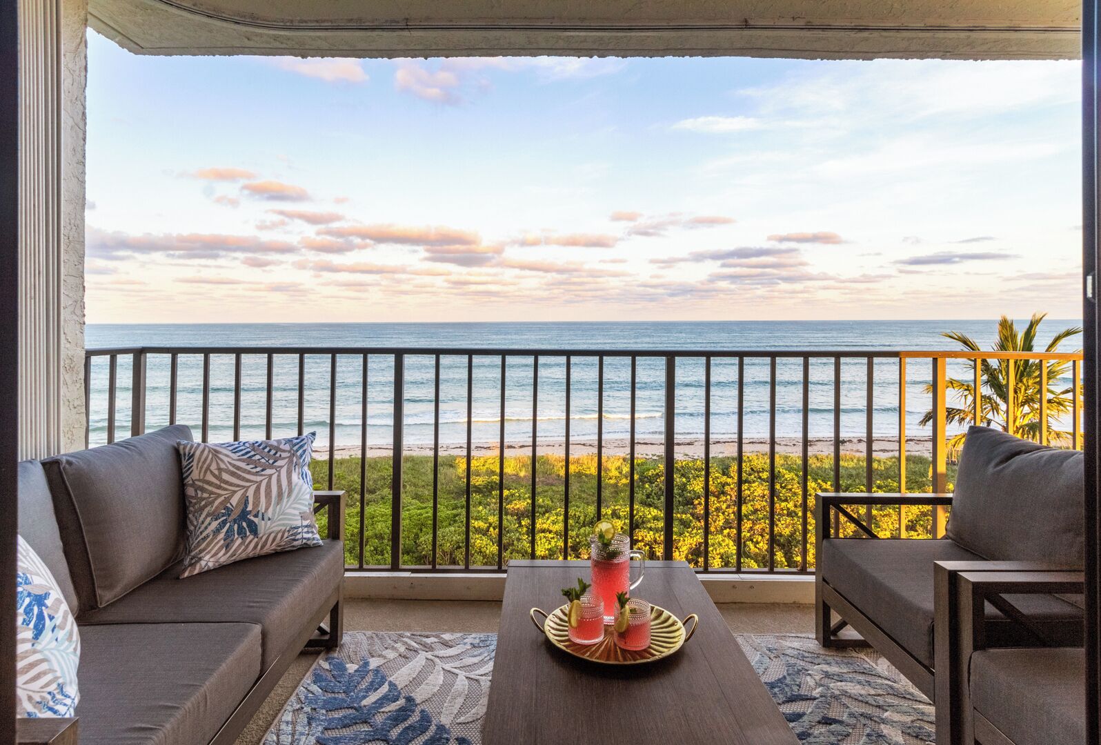 Varanda com vista para o oceano, um sofá, uma mesa com bandeja para bebidas e um corrimão.