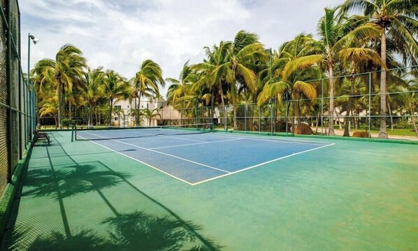 Ein Tennisplatz, umgeben von Palmen und einem Gebäude.