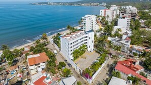 Une zone urbaine côtière, avec un imposant bâtiment blanc à plusieurs étages, entouré de constructions plus petites et de palmiers.