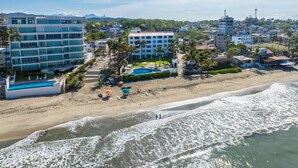 Un hôtel situé sur la côte, avec plusieurs étages, une plage équipée de parasols et une piscine.