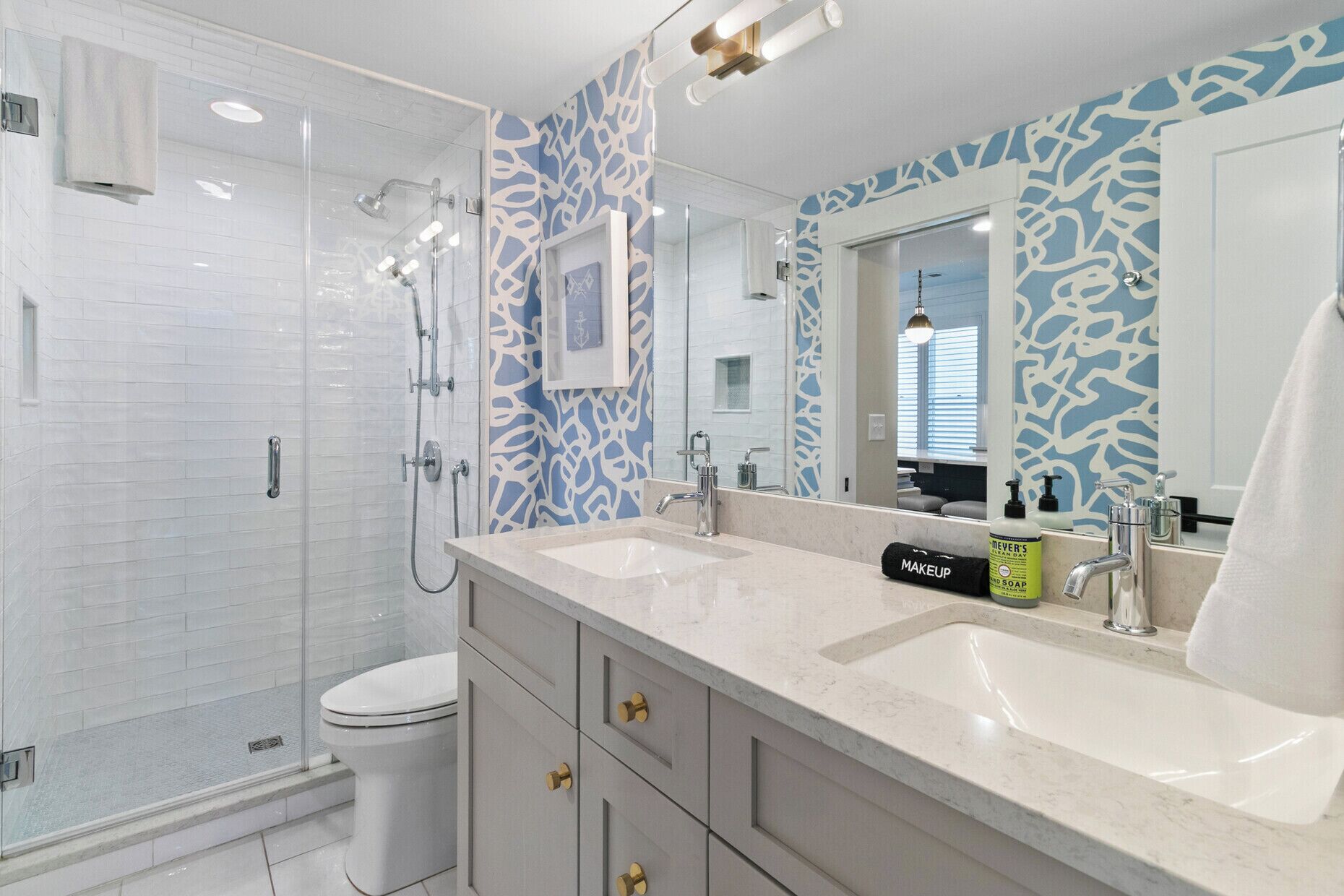 A modern bathroom with two sinks, a walk-in shower, and a toilet.