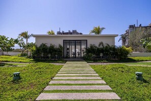 Ein modernes Gebäude mit einer zentralen Glasfassade und einem symmetrischen Garten mit einem Steinweg, der zum Eingang führt.