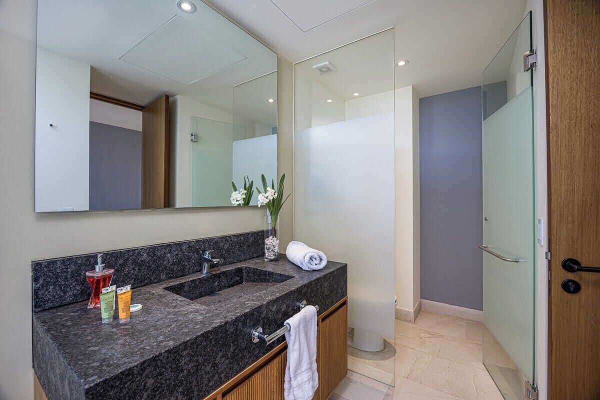 A modern bathroom with a granite countertop, a large mirror, and a glass shower enclosure.