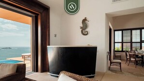 A modern room with a large window overlooking a pool and the sea, a black reception desk, wicker furniture, and a decorative seahorse on the wall. - 4 BR Penthouse - Breathtaking Views - Private Pool (Zihuatanejo)