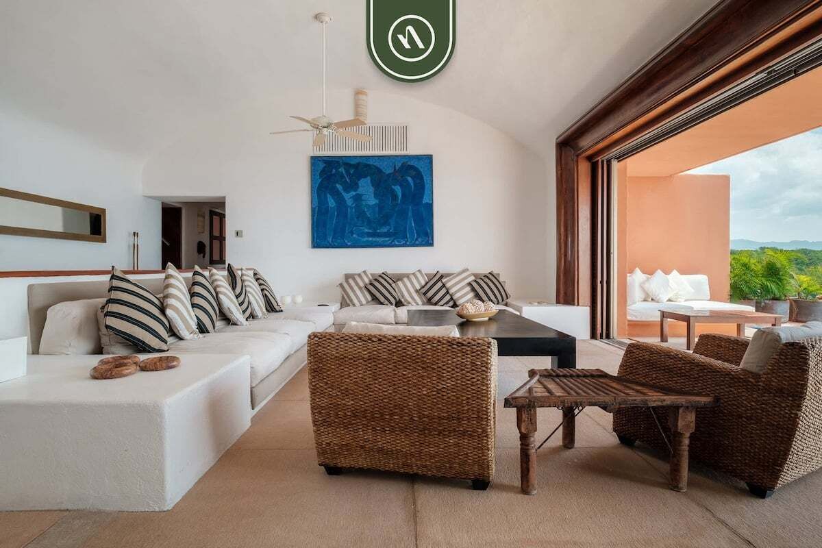 A modern living room with a white sofa, wicker chairs, a coffee table, and a painting on the wall.