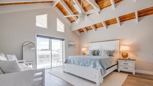 A bedroom with a large bed, a ceiling fan, a nightstand, and a view of the outdoors.