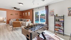 Ein Zimmer mit Fußballtisch, einer Couch, Deckenventilator und Bücherregal.