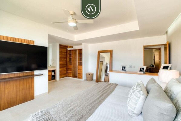 A modern bedroom with a large bed, a TV, a ceiling fan, and a wooden wardrobe.