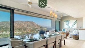 Un espace repas moderne avec une table en verre, des chaises blanches et une vue sur un paysage montagneux.